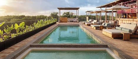 A rooftop pool with a checkered edge, lounge chairs, and a covered seating area.