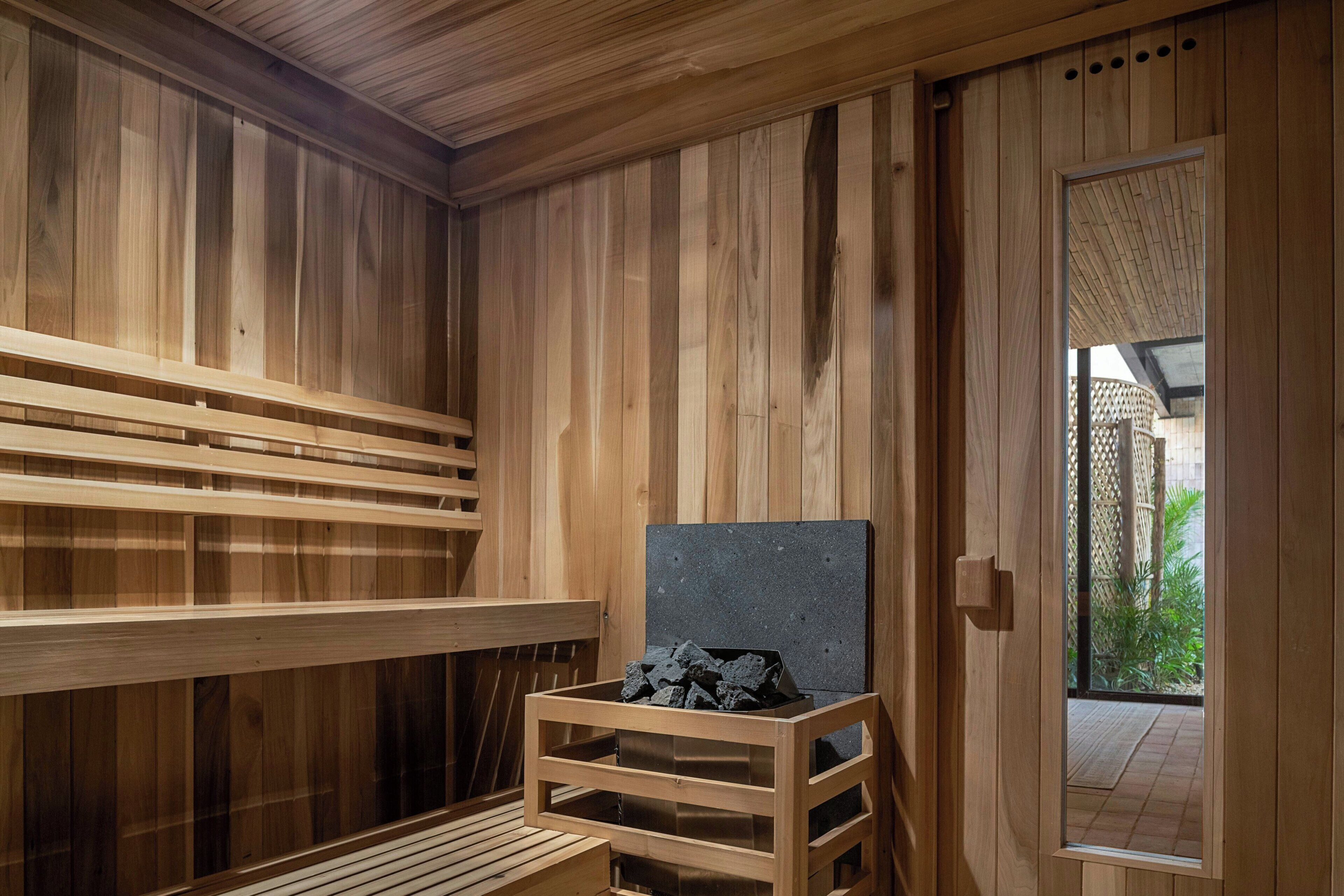 Un sauna en bois avec des bancs, un banc en pierre et une porte donnant sur l’extérieur.