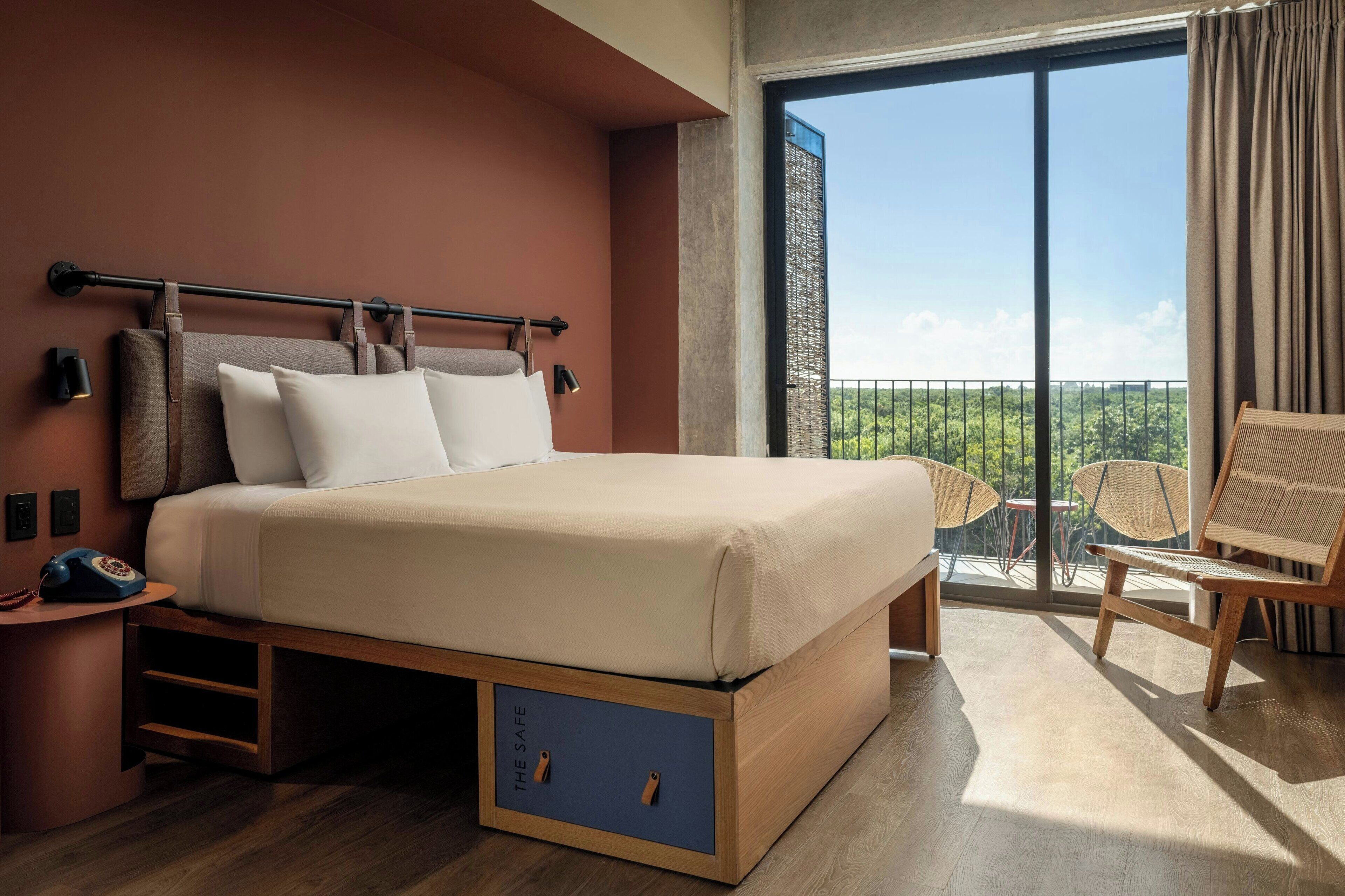 A bedroom with a bed, bedside tables, a telephone, and a view of the outdoors.
