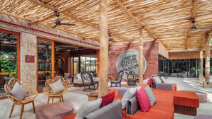 Un espace de détente intérieur avec des fauteuils et des canapés en osier, un plafond en bambou et une grande fresque représentant un léopard.