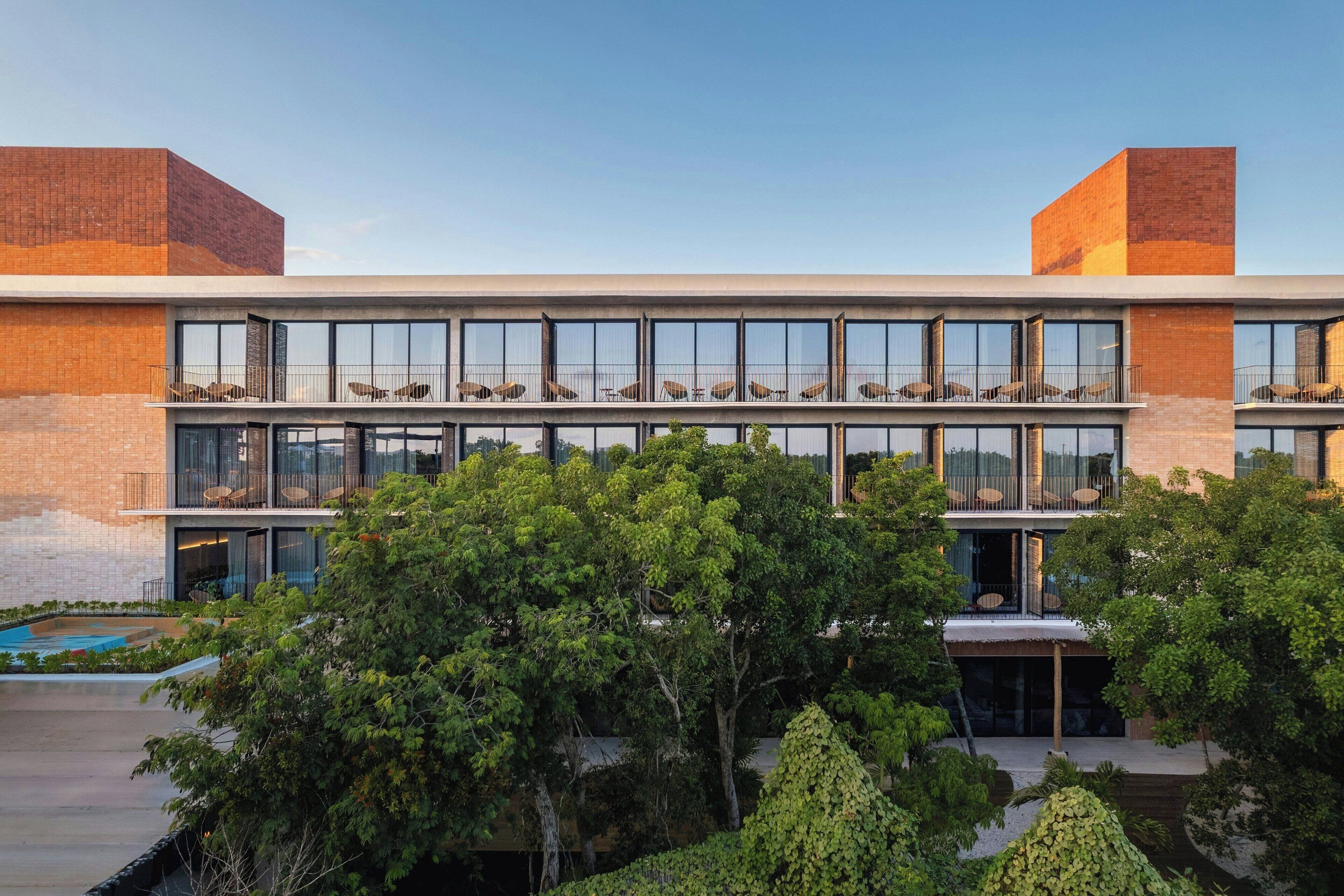 Een modern gebouw met een plat dak, grote ramen en een binnentuin met bomen.