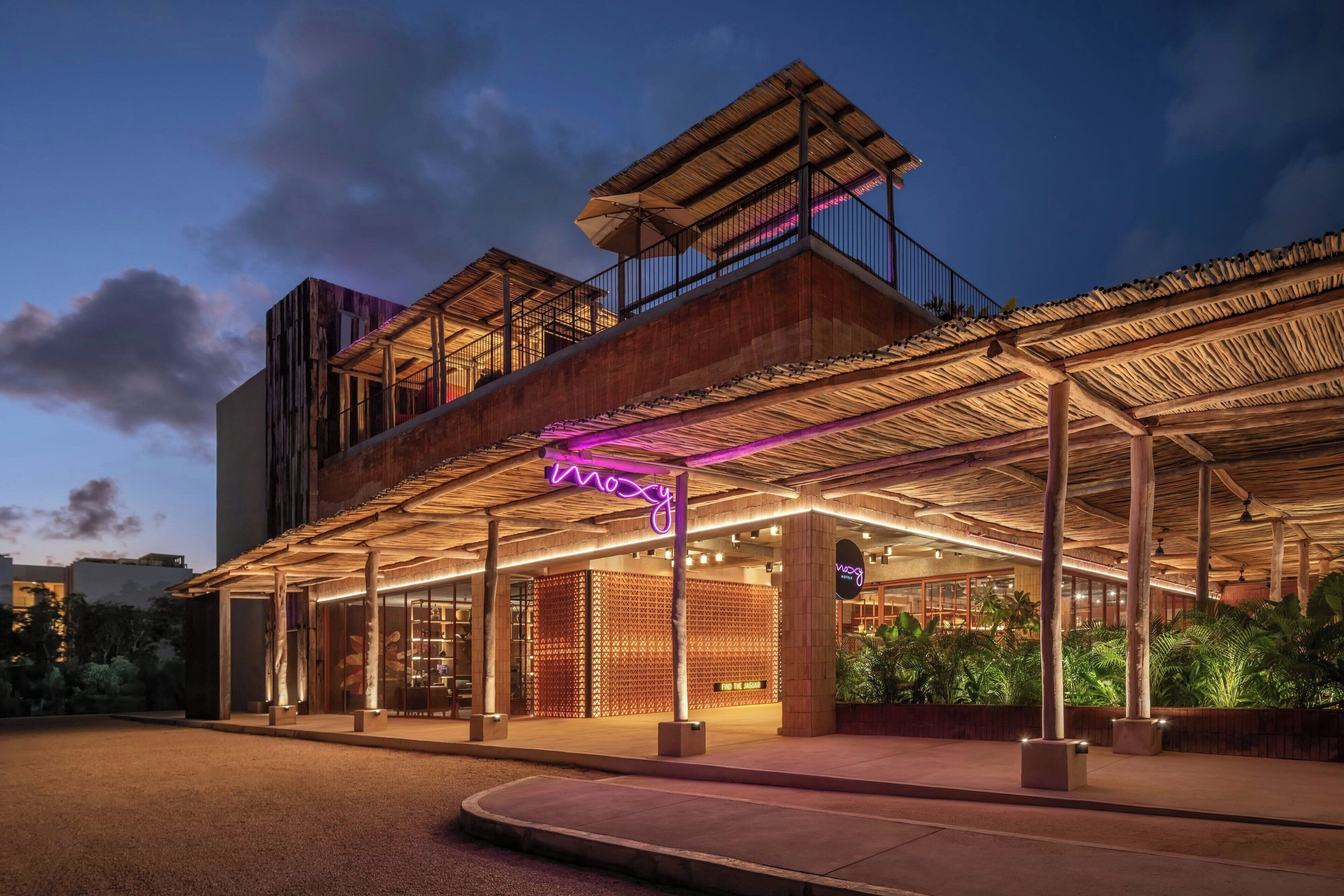 A modern hotel with a covered outdoor area, a neon sign, and a rooftop terrace.