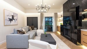 A modern living room with a grey sofa, a white armchair, a black coffee table, and a chandelier. - Luxury 5BR Poolhouse & Theater - 2mins to BTS (Bangkok)