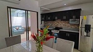 Una cocina moderna con armarios oscuros, un refrigerador de acero inoxidable y un comedor con mesa y sillas de mármol.