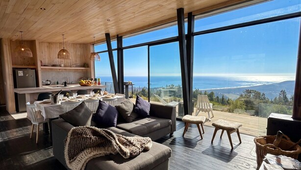 A modern interior with a dining area, a sofa, and a view of the ocean. - Olas de Buchupureo - con vida de campo (Buchupureo)