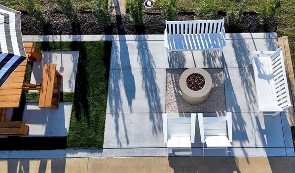 Un espace patio aménagé avec une table et des chaises en bois, un banc blanc et un jardinière circulaire.