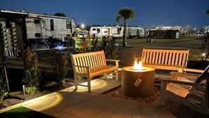 A patio area with a fire pit and benches, surrounded by a grassy area and a parking lot with RVs.
