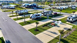 Un camping con vehículos recreativos estacionados en zonas verdes cuidadas, una mesa de picnic y un área de estar techada.