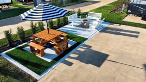 Un espace pique-nique équipé d’une table et de bancs en bois, d’un foyer et d’un parasol à rayures.