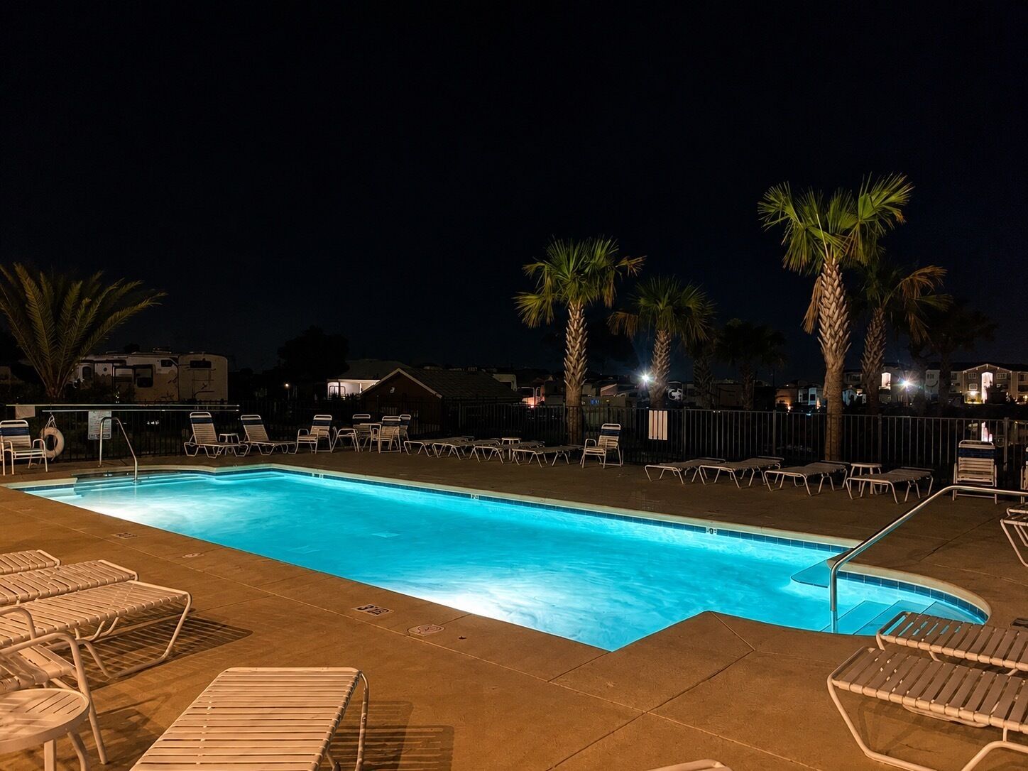 Une piscine avec des chaises longues et des palmiers, le tout illuminé la nuit.