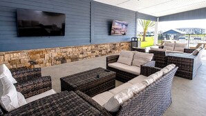 An outdoor seating area with wicker furniture, a stone wall, and a mounted television.