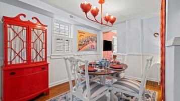 A dining area with a round table set for four, white chairs with striped cushions, a red cabinet, and a wall-mounted light fixture.