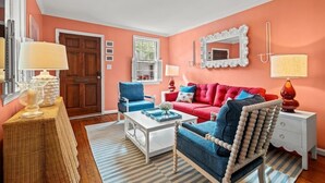 A living room with a red sofa, blue armchair, white coffee table, and a white side table with lamps.
