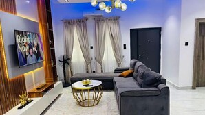 A modern living room with a sofa, a coffee table, and a TV on the wall. - Madisonville Apartment  (Abuja)