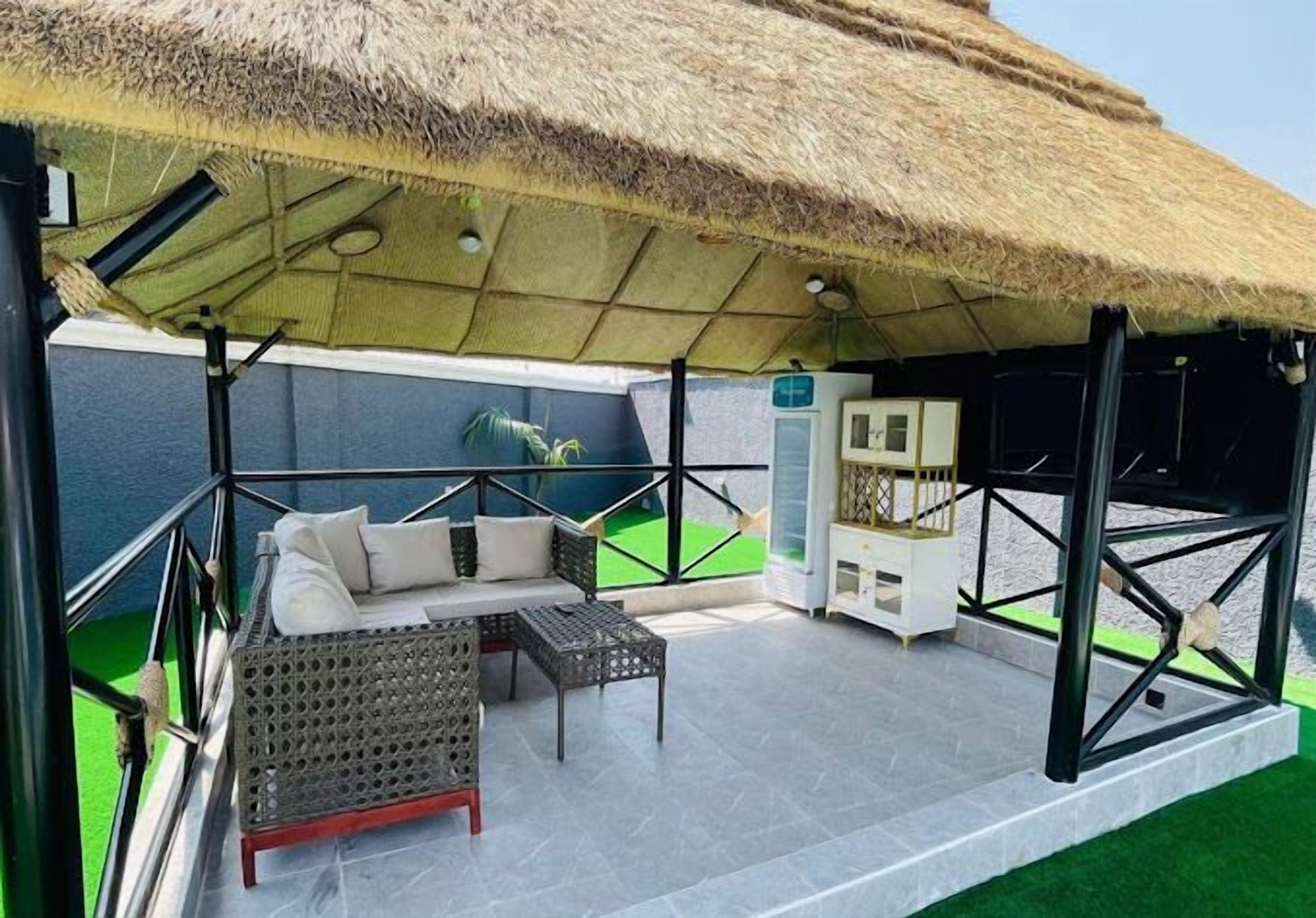 A covered outdoor seating area with a thatched roof, a sofa, and a small table.