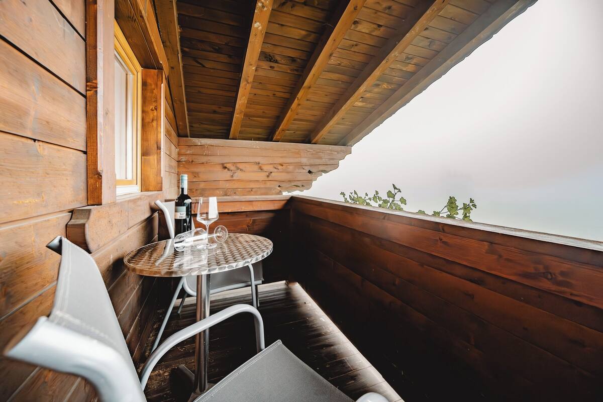 A wooden cabin with a small balcony, a round table with two chairs, and a bottle of wine.