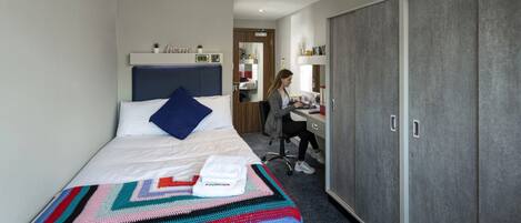 A hotel room with a bed, a desk, and a wardrobe.