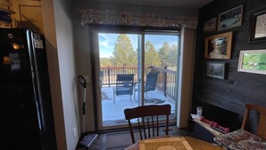 A kitchen with a refrigerator, a dining table with a placemat, a chair, and a sliding glass door leading to a deck with outdoor furniture.