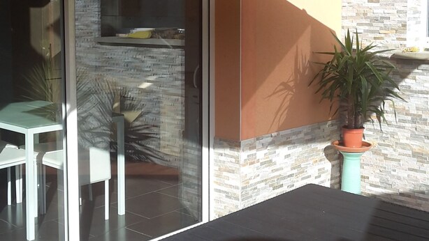 An outdoor patio area with a yellow umbrella, a glass door leading to a dining area, and a potted plant. - Apartment T2 - 40M² (40M²) (Saint-Martin-de-Seignanx)