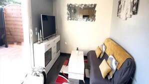 A living room with a sofa, TV, and a small table. - Apartment T2 - 40M² (40M²) (Saint-Martin-de-Seignanx)