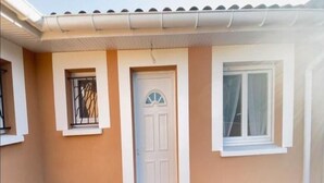 A house with a white door, a small window with a metal grille, and a larger window with a white frame. - Apartment T2 - 40M² (40M²) (Saint-Martin-de-Seignanx)