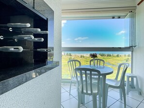 A balcony with a view of the beach, a grill, and a table with chairs. - Resid. Clube Mar Grosso-Laguna - LAG100 (Laguna)