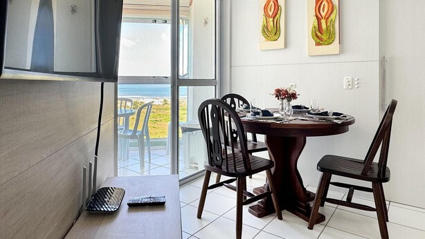 A dining area with a table set for two, two chairs, a remote control on a side table, and artwork on the wall. - Resid. Clube Mar Grosso-Laguna - LAG100 (Laguna)