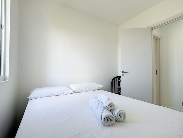 Una habitación limpia y blanca con una cama, una puerta y un ventanal.