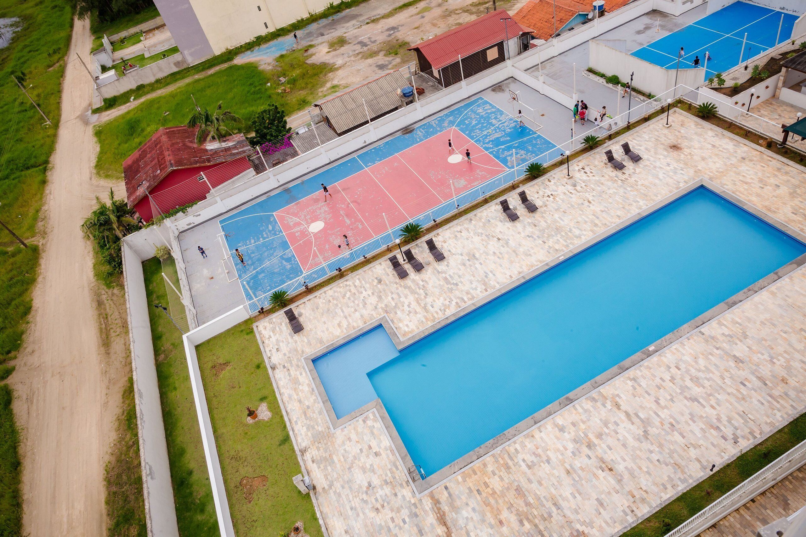 Vista aérea de un hotel con una amplia piscina, cancha de tenis y una zona cubierta con asientos.