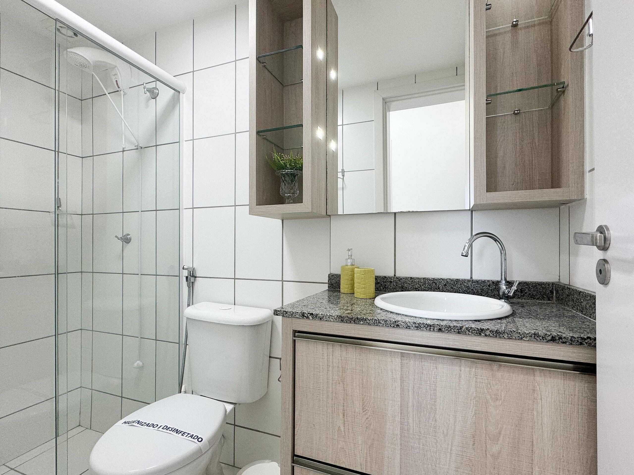 Une salle de bain moderne avec une douche à l’italienne en verre, des toilettes blanches, un comptoir en granit et un meuble en bois.