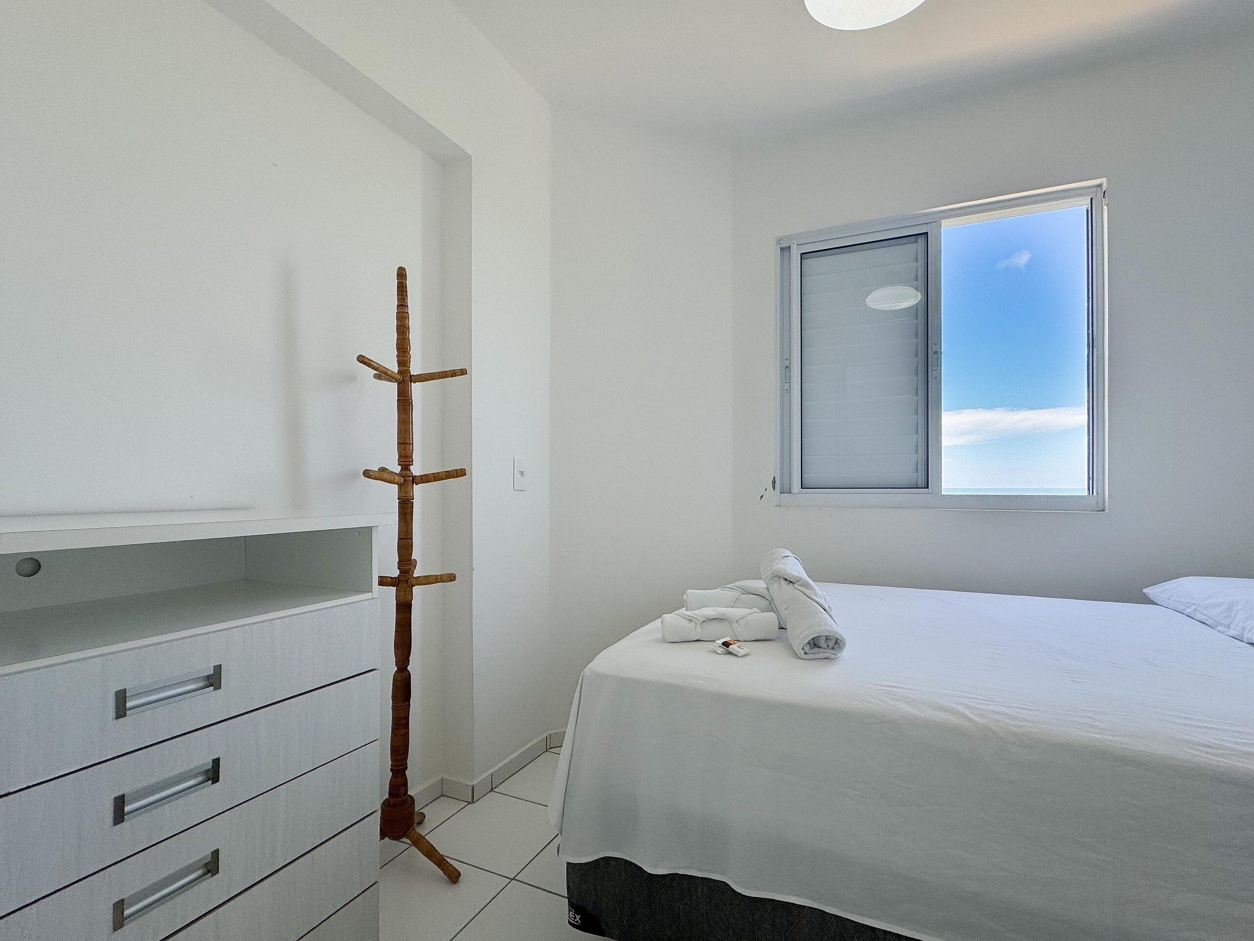 Habitación de hotel con cama, armario, perchero y ventana con vista al cielo.