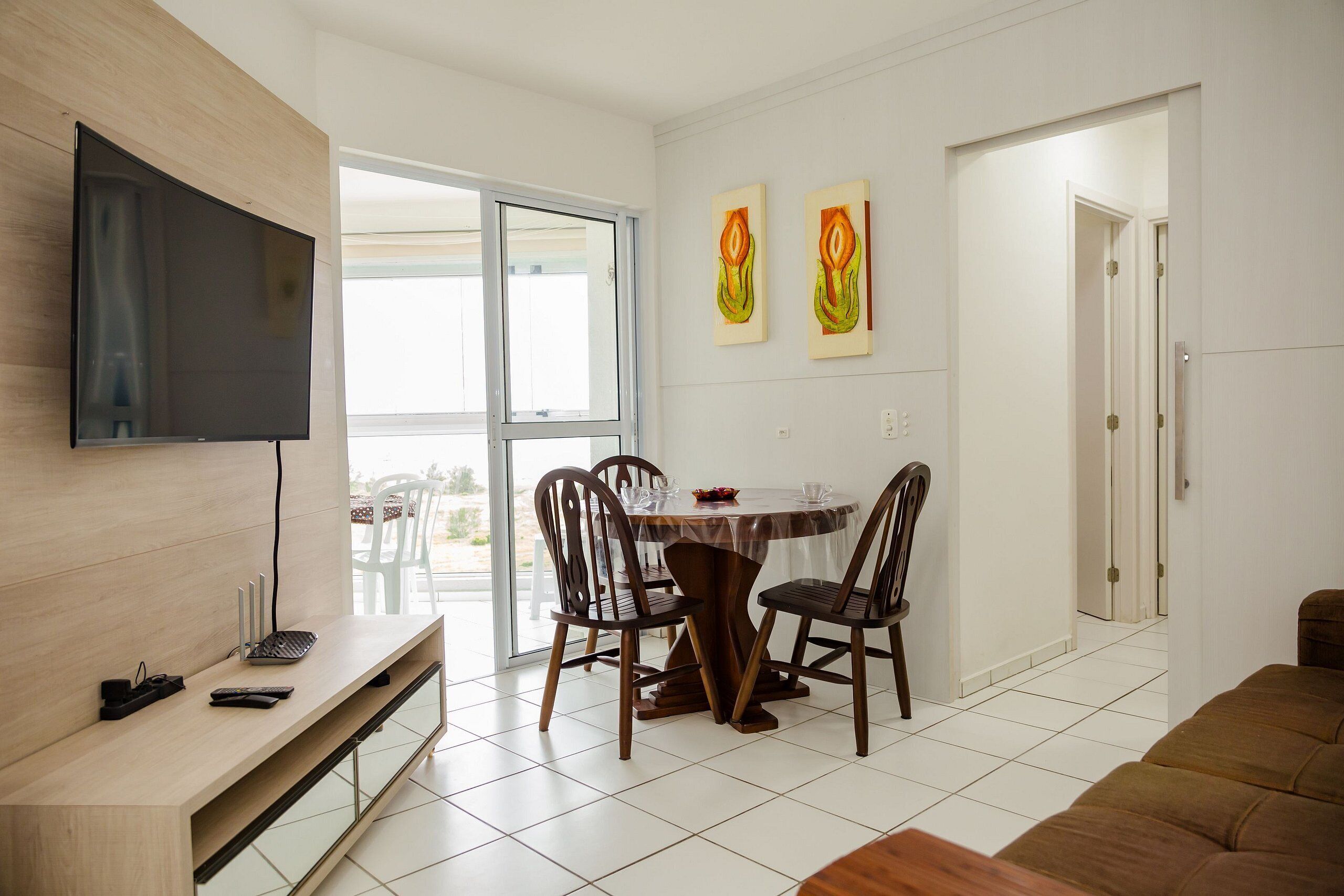 A modern living room with a flat-screen TV, a dining table with chairs, and a sofa.