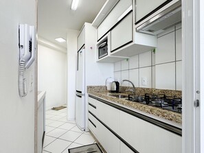 Een moderne keuken met witte kasten, een granieten aanrecht, een inbouwfornuis en een magnetron.