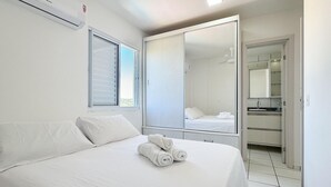 A hotel room with a bed, a large mirror, a wardrobe, and a window with blinds. - Resid. Clube Mar Grosso-Laguna - LAG100 (Laguna)