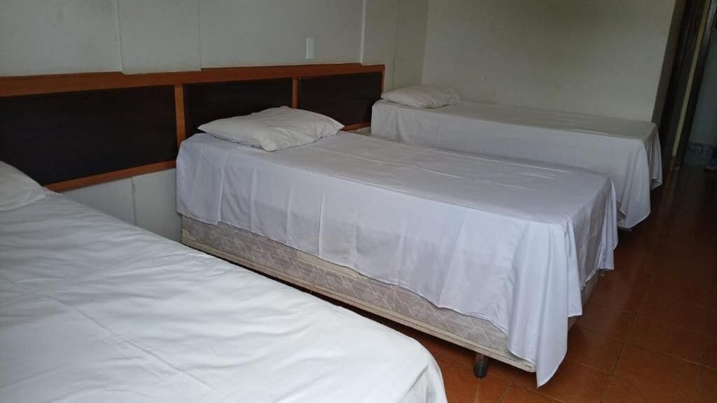 Ein Zimmer mit drei Einzelbetten an der Wand, jeweils mit Holz Kopfteil und weißer Bettwäsche.