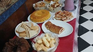 A buffet table with various food items, including bread, pastries, and a cake. - Gutemberg Palace Hotel (Nova Serrana)