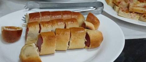Una mesa de comedor con diversos platos, incluyendo pan, un perro caliente y una pizza.