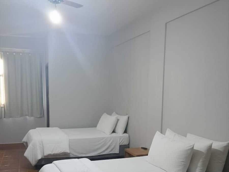 Una habitación con dos camas, un ventilador de techo y una ventana con cortinas.