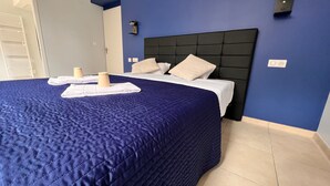 Un lit bien fait, recouvert d’une couette bleu foncé, de draps blancs et de deux oreillers beige.