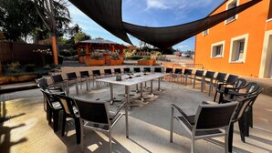 Une terrasse extérieure avec une longue table et des chaises, entourée de jardinières et d’une pergola en bois.