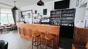 Un espace bar avec des tabourets en bois, un appareil à café et des étagères remplies de verres et de bouteilles.