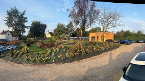 Un quartier résidentiel avec des maisons, des voitures garées et un jardin agrémenté de plantes en fleurs.
