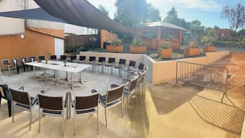 Un patio al aire libre con una mesa redonda y sillas, rodeado por un muro bajo y una zona con sombra.
