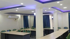 Μια αίθουσα συνεδριάσεων με πολλά τραπέζια και καρέκλες, λευκούς τοίχους και μπλε κουρτίνες.