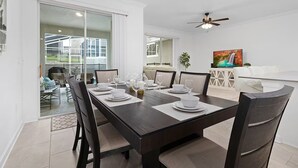 A dining area with a dark wooden table set for four, white chairs, and a glass partition separating the dining area from a living room. - FL- 1042 Splash Shot (Davenport)