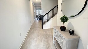 A hallway with a staircase, a round mirror, a potted plant, and a cabinet. - FL- 1042 Splash Shot (Davenport)