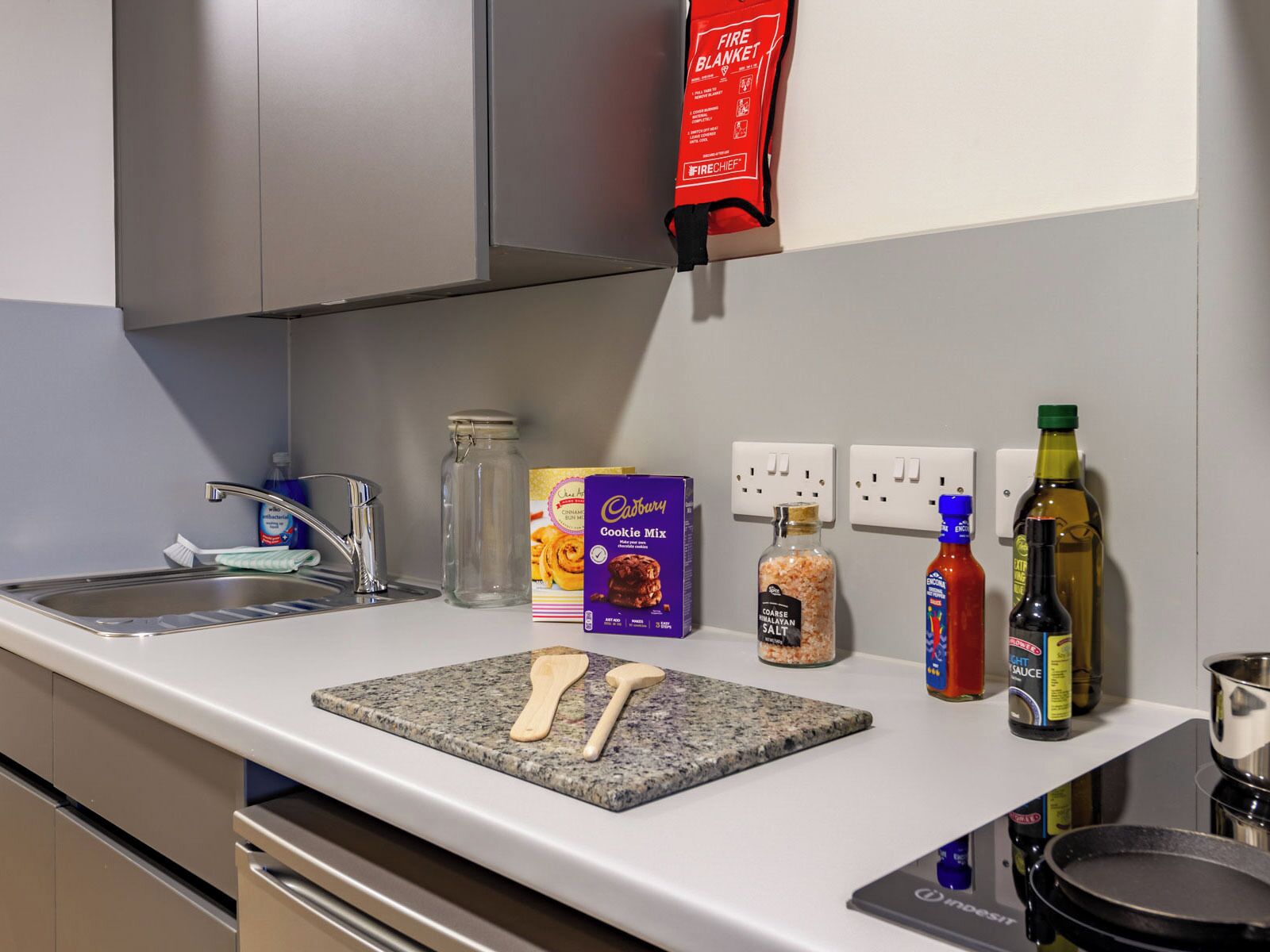 A kitchen with a granite countertop, a sink, a fire blanket, a cookie mix box, a salt container, and cooking oil bottles.