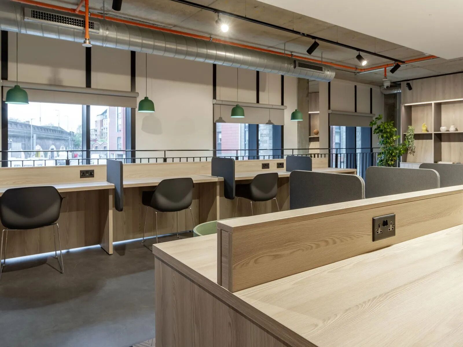 A modern office space with wooden desks, black chairs, and green pendant lights.