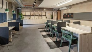 Un espacio de oficina moderno con mesas largas y sillas, una alfombra estampada y un tablón de anuncios en la pared.