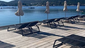 A wooden deck with lounge chairs and umbrellas overlooking a calm lake with hills in the background.